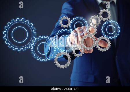 Geschäftsmann berührt Zahnradmechanik auf dunklem Hintergrund, Nahaufnahme Stockfoto