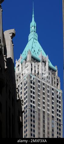 Ein markanter Art déco-Wolkenkratzer mit türkisfarbenem Turm erhebt sich vor einem leuchtend blauen Himmel und zeigt Manhattans legendäre Skyline und historische Architektur Stockfoto
