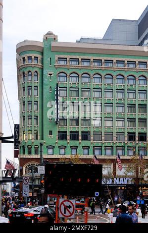 Das Hotel Stratford mit seiner grünen Fassade an einer belebten Straße am Union Square, San Francisco, bietet Fußgänger, amerikanische Flaggen und urbane Aktivitäten. Stockfoto