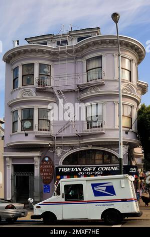 Eckgebäude im viktorianischen Lavendelstil mit Erkerfenstern und einem USPS-Truck, der vor einem tibetischen Souvenirladen in San Franciscos Viertel Haight geparkt ist Stockfoto