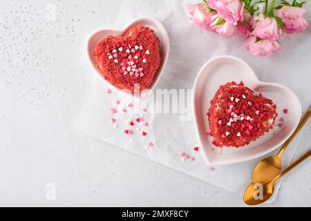 Zwei Kuchen Roter Samt in Form von Herzen auf weißem Teller, Rosenblumen und eine Tasse Kaffee auf rosafarbenem romantischem Hintergrund. Dessert-Idee für den Valentinstag, Stockfoto