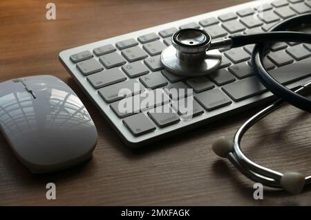 Stethoskop, Maus und Computertastatur auf Holzhintergrund. Konzept der Medizinischen Informationstechnik und Computerdiagnostik und -Reparatur. Stockfoto