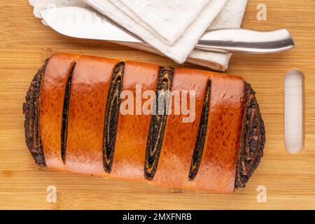 Eine köstliche Mohnrolle auf Bambusbrett mit weißer Serviette und Messer, Makro, Draufsicht. Stockfoto