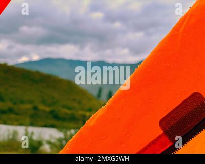 Am Rand der Markise des orangefarbenen Zelts vor dem Hintergrund des Flusses und der Berge in Altai liegen Regentropfen. Stockfoto