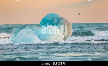 Die Welle stürzt gegen einen kleinen Eisberg, der im Meer schwebt Stockfoto
