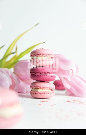 Stapel rosafarbener Makronen mit rosafarbenen Tulpen auf weißem Hintergrund Stockfoto