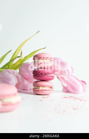 Stapel rosafarbener Makronen mit rosafarbenen Tulpen auf weißem Hintergrund Stockfoto