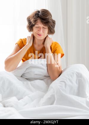 Schläfrige Frau im gelben Pyjama massiert sich den Hals. Ich wache früh am Morgen auf. Die Frau schläft genug. Stockfoto
