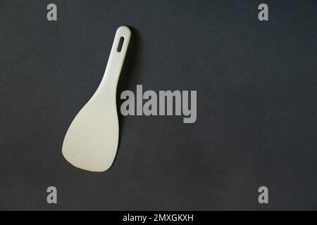 Weißer Kunststofflöffel für Multicooker auf dunklem Hintergrund Stockfoto