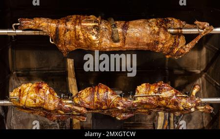 Lamm auf gegrillten Spießen mit heißer Holzkohle. Das Lamm wird komplett auf einem Spieß auf dem Feuer gekocht. Kochen. Stockfoto