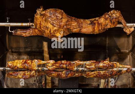 Lamm auf gegrillten Spießen mit heißer Holzkohle. Das Lamm wird komplett auf einem Spieß auf dem Feuer gekocht. Kochen. Stockfoto