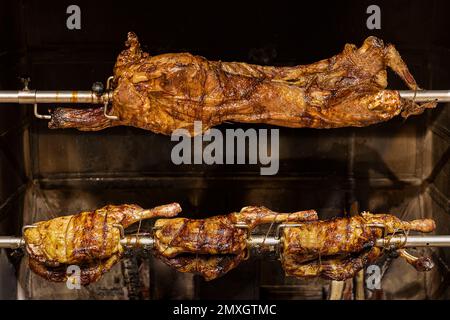 Lamm auf gegrillten Spießen mit heißer Holzkohle. Das Lamm wird komplett auf einem Spieß auf dem Feuer gekocht. Kochen. Stockfoto