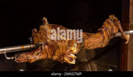 Lamm auf gegrillten Spießen mit heißer Holzkohle. Das Lamm wird komplett auf einem Spieß auf dem Feuer gekocht. Kochen. Stockfoto