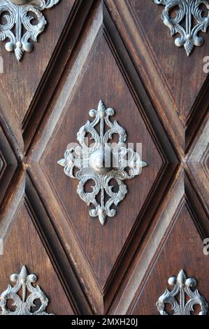 Altes Holztor mit Metalldekor auf Holzwürfeln. Detail einer Tür aus braunem Holz mit silbernen Motiven mit viel Kunst. Highlight für den Knopf Stockfoto