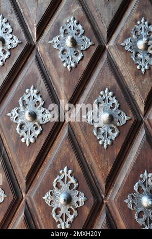 Altes Holztor mit Metalldekor auf Holzwürfeln. Detail einer Tür aus braunem Holz mit silbernen Motiven mit viel Kunst. Highlight für den Knopf Stockfoto