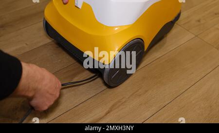 Ein weißer Mann, der das Kabel des Staubsaugers in seinem Lager verpackt hat. Angry man versucht, ein verklemmtes Kabel in den Staubsauger zu packen. Stockfoto