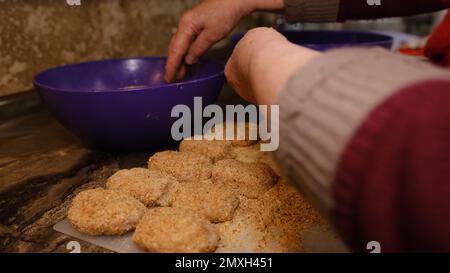 Alte Seniorin, die in der Küche Koteletts kocht. Hausgemachte Koteletts von der Großmutter aus Zwiebelfleisch Stockfoto
