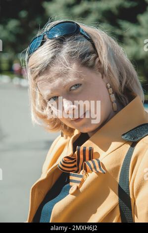 KOLOMNA, Region Moskau, Russland 9. Mai 2014. Porträt einer jungen Frau in einem gelben Mantel mit einem St. Das George-Band bei der Vorbereitung des marschs Stockfoto