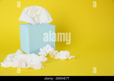 Gebrauchte Papiertücher und Schachtel auf gelbem Hintergrund. Platz für Text Stockfoto
