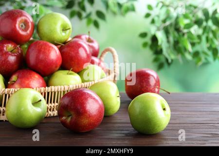 Saftige rote und grüne Äpfel in Korbschale auf Holztisch im Freien Stockfoto