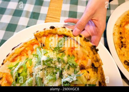 Weibliche Hände, die Scheiben von authentischer italienischer caesar-Steinpizza mit Rucola, Sauce, gegrilltem Hähnchen, Kräutern und würzigem Parmesankäse nehmen. Stockfoto