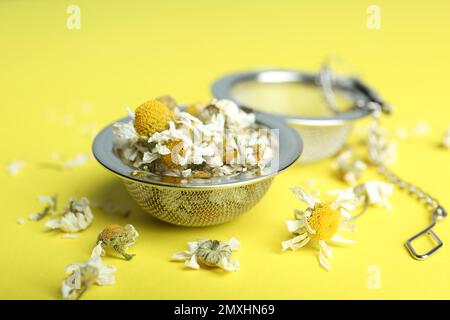 Trockene Kamillenblüten im Infusor auf gelbem Hintergrund, Nahaufnahme Stockfoto