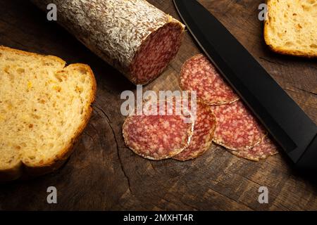 Ungarische Salami mit Kornbrotscheiben auf rustikalem Holzhintergrund. Stockfoto