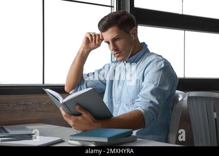 Ein Mann, der am Tisch im Café Hörbücher hört Stockfoto