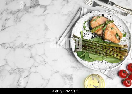 Leckeres Lachssteak mit gegrilltem Spargel auf einem weißen Marmortisch, flach liegend. Platz für Text Stockfoto