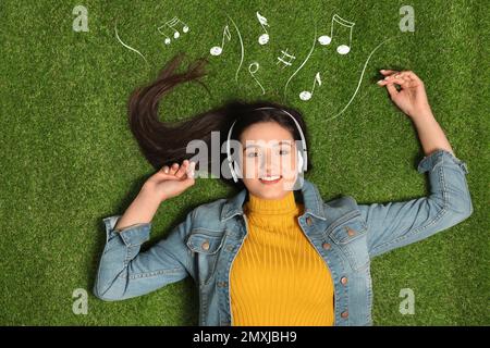 Junge Frau, die Musik über Kopfhörer auf grünem Gras hört, Draufsicht Stockfoto