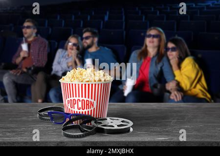 Popcorn, 3D Gläser, Filmrolle auf dem Tisch und junge Leute im Kino Stockfoto