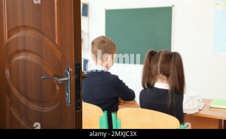 Holztür öffnet sich in ein modernes Klassenzimmer mit Schülern, Bannerdesign Stockfoto