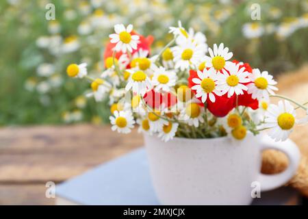 Becher mit Kamillen und Mohn auf dem Tisch im Freien Stockfoto