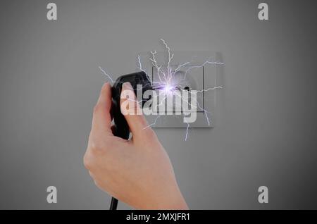 Eine Frau, die beim Ausstecken einen elektrischen Schlag erleidet, eine Nahaufnahme Stockfoto