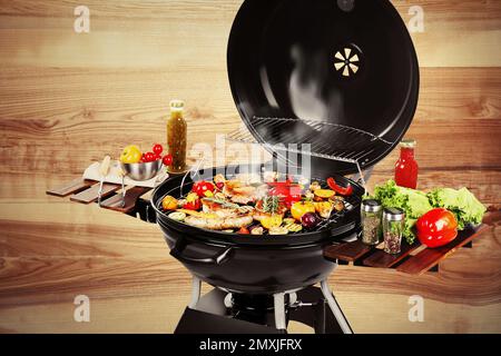 Barbecue-Grill mit Fleischprodukten und Gemüse auf Holzhintergrund, Nahaufnahme Stockfoto