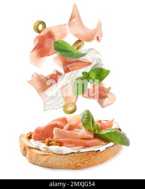 Leckeres Bruschetta mit fliegenden Zutaten auf weißem Hintergrund Stockfoto