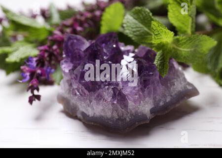 Amethystischer Edelstein und Heilkräuter auf weißem Holztisch, Nahaufnahme Stockfoto