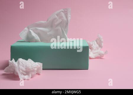 Schachtel mit Papiertüchern und gebrauchten, zerknitterten Servietten auf pinkfarbenem Hintergrund Stockfoto