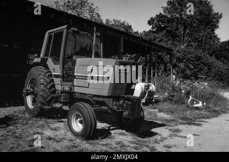 Ein moderner internationaler Traktor, der vor einer Scheune im Gras auf einem Bauernhof geparkt ist. Littleton Massachusetts. Das Bild wurde in analogem Schwarzweiß aufgenommen Stockfoto