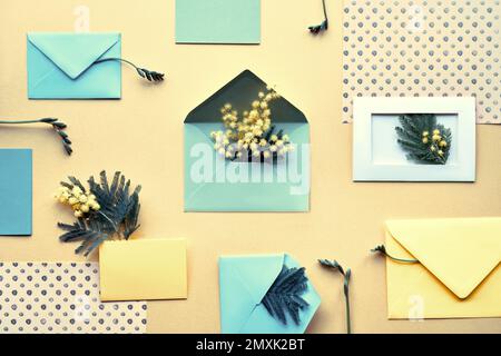 Mimosablüten, mintgrüne Umschläge und farbiges Papier auf gelbem Hintergrund. Knolling, ordentlich gestaltete Einrichtung im Frühling. Flach liegend, Draufsicht. Stockfoto