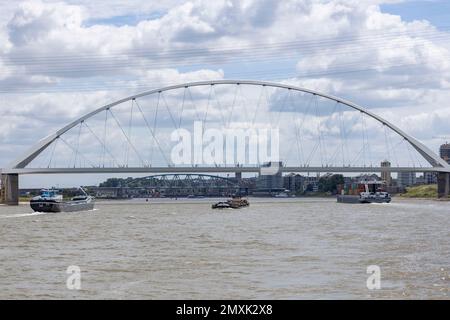 Frachtboote, die unter der Waalbrug-Brücke vorbeifahren und vom Wasser aus gesehen werden. Stockfoto