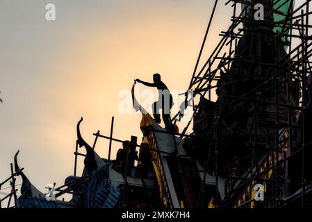 Wat Yannawa, Bangkok, Thailand, 18. Januar 2023: Silhouette der Bauarbeiter auf einem Tempeldach, der goldene Giebelspitzen repariert. Stockfoto