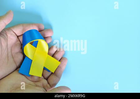 Menschliche Hände mit blauem und gelbem zweifarbigem Band auf blauem Hintergrund. World Down Syndrome Day, Awareness, Help and Support Konzept. Stockfoto