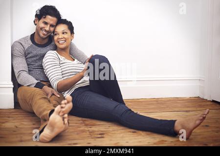 Ein süßes Heim mit meiner Liebe. Die volle Länge eines liebevollen Paares, das zu Hause auf dem Boden sitzt. Stockfoto