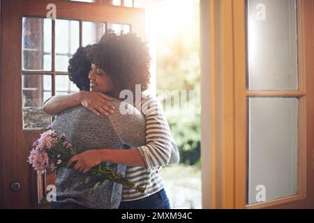 Er gibt ihr immer das Gefühl, etwas Besonderes zu sein. Eine junge Frau umarmt ihren Mann, nachdem sie Blumen von ihm erhalten hatte. Stockfoto