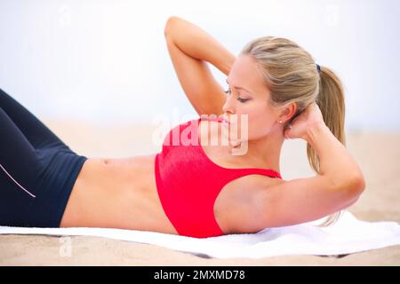 Mach die bauchmuskeln an. Eine junge Frau in Sportbekleidung, die am Strand situps macht. Stockfoto