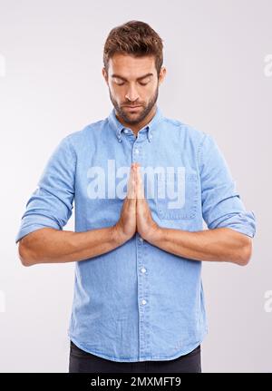 Frieden finden. Studioaufnahme eines gutaussehenden jungen Mannes, der vor grauem Hintergrund betet. Stockfoto