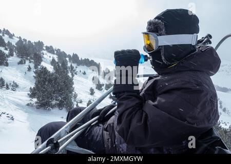 Skifahrer erschöpft und Trinkwasser aus einer Flasche, während sie die Skipisten mit dem Sessellift besteigen. Stockfoto