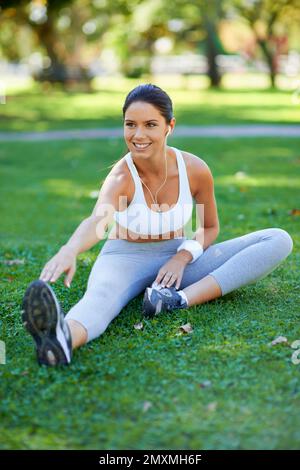 Sie weiß, wie wichtig Dehnübungen sind. Eine wunderschöne junge Frau, die sich im Park streckt. Stockfoto