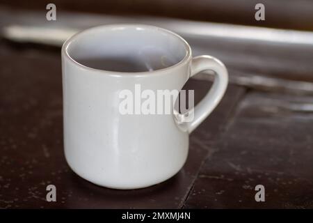 Liebe am Morgen: Ein weißer Becher mit herzförmigem Griff auf einem Holztisch aus nächster Nähe Stockfoto